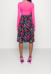 Top rosa trasparente a maniche lunghe abbinato a una gonna nera a stampa floreale con fiori rossi e blu. Accessoriato con tacchi a strappo rosa.