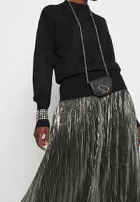 Suéter de punto negro con mangas largas y puños acanalados, combinado con una falda plisada plateada y un pequeño bolso cruzado negro con cadena.