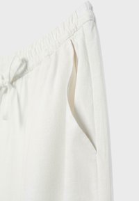 Pantalon léger en lin blanc avec taille élastique à cordon et poche latérale sur un fond clair.