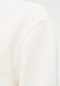 Υφασμα πλεκτό με υφή σε ανοιχτό μπεζ χρώμα, με ανοιχτή εφαρμογή, εμφανείς ραφές και απαλό, άνετο ύφος.