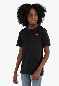 Svart bomulls T-skjorte med korte ermer, rund hals og med en liten r�ød Levi's-logo på venstre bryst. Brukt sammen med lyseblå jeans.
