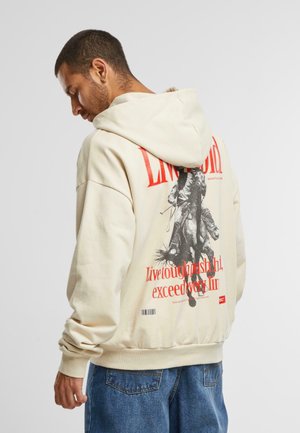 Felpa beige con una grande stampa grafica sul retro che raffigura un cavallo e un cavaliere, arricchita da testo rosso. Tessuto in misto cotone, vestibilità comoda.