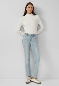 Weißer gerippter Rollkragenpullover, hellblaue Jeans und beigefarbene Sneakers mit weißen Akzenten. Einfaches Design, taillierte Passform und gerade Beinform.