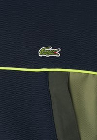 Pólo em tecido azul-marinho com um logo de crocodilo verde com detalhes em vermelho, destacado por um detalhe em piping verde-lima e um design texturizado.