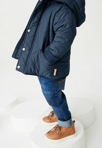 Námořnická prošívaná bunda s kapucí a patentkami, spárovaná s modrými džíny a světlými šněrovacími botami s bílou podrážkou. Texturované detaily látky.