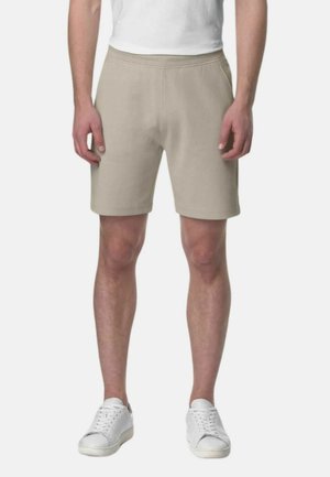 Shorts di cotone beige con elastico in vita, caratterizzati da una vestibilità rilassata e una superficie liscia. Indossati con sneakers bianche.