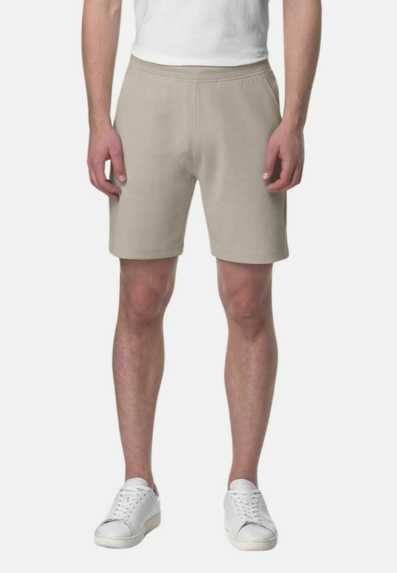 Shorts di cotone beige con elastico in vita, caratterizzati da una vestibilità rilassata e una superficie liscia. Indossati con sneakers bianche.