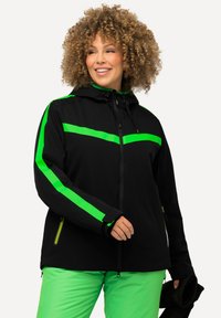 Schwarze Jacke mit leuchtend grünen Streifen, Reißverschluss und verstellbarer Kapuze. Kombiniert mit grünen Hosen, die ein modernes Design und eine sportliche Passform zeigen.