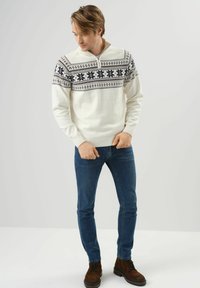 Biały sweter dzianinowy z wzorzystym granatowym karczkiem, pół-zamek przy dekolcie; w komplecie z ciemnoniebieskimi dżinsami i brązowymi butami na sznurówki.