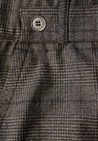 Gros plan sur un tissu à carreaux gris et noir avec un bouton et un détail de poche cousue sur un vêtement.