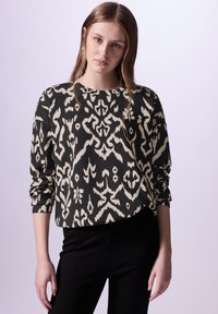 Pullover a maniche lunghe nero e crema con motivo, caratterizzato da un collo rotondo e una vestibilità comoda. Abbinato a pantaloni neri.