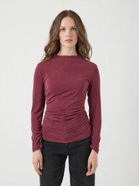 Langermige, burgundy top gemaakt van zacht materiaal met een gedrapeerd ontwerp en geplooide details aan de zijkanten, gecombineerd met donkere jeans.