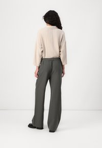 Bež, teksturirana dolga majica z dolgimi rokavi v kombinaciji z zelenimi širokima hlačami s črtami. Obleka ima elastičen pas in sproščen kroj.