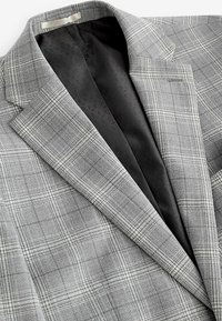 Blazer de cuadros gris con un exterior tejido texturizado, forro de satén negro y solapas muestradas. Incluye un patrón de cuadros detallado.