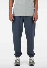 Pantalones de chándal azul oscuro con puños elásticos y cintura con cordón, combinados con una camiseta gris y zapatillas deportivas grises. Diseño sencillo, ajuste cómodo.
