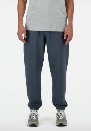 Pantalones de chándal azul oscuro con puños elásticos y cintura con cordón, combinados con una camiseta gris y zapatillas deportivas grises. Diseño sencillo, ajuste cómodo.