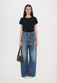 Marineblauwe katoenen t-shirt gecombineerd met lichtblauwe, wijde denim jeans met een hoge taille en een riem. Een zwarte handtas en witte schoenen maken de look af.