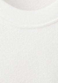Gros plan sur un tissu blanc côtelé montrant l'encolure arrondie et la texture tricotée d'un vêtement.