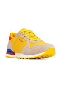 Chaussures de sport jaunes avec une tige en daim et en synthétique, dotées d'un embout beige, d'accents bleus et rouges, et d'une semelle extérieure en caoutchouc texturé.