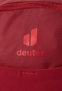Red fabric with a textured finish featuring the "deuter" logo in a lighter shade. Includes stitching detail along the edges.