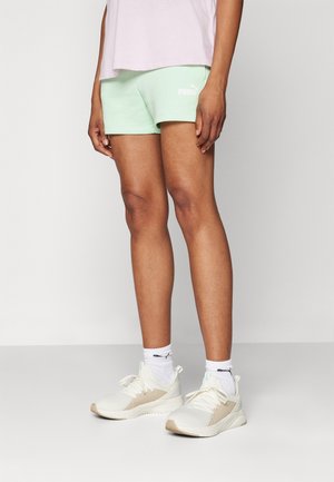 Person wearing light mint green Puma shorts, white ankle socks, and beige Puma sneakers, standing against a plain light background.