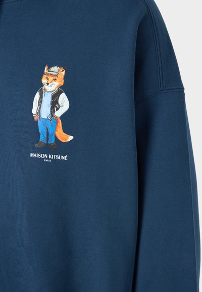 Sweatshirt bleumarin cu un grafic de vulpe desenată în stil cartoon, îmbrăcată casual. Textul "MAISON KITSUNÉ PARIS" imprimat sub imagine. Textură netedă.