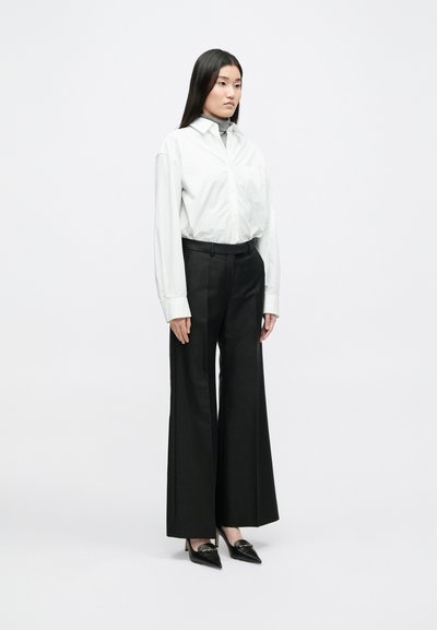 Λευκό πουκάμισο με μακριά μανίκια και φαρδείς γιακάδες, γκρι ζιβάγκο από κάτω, μαύρες παντελόνες με ψηλή μέση και φαρδιά πόδια, και μαύρα μυτερά παπούτσια.