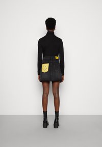 Maglione collo alto nero e gonna di jeans con dettagli di tasca a faccina gialla. La gonna presenta un'etichetta in vita e si abbina a stivali neri alti fino al ginocchio.