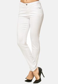 Jeans blancos de corte slim con una textura suave, cierre de botón y bolsillos frontales, combinados con tacones altos negros de punta afilada.