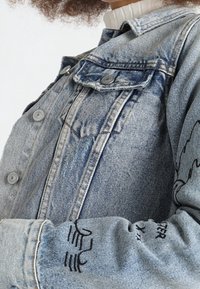 Jeansjacka i ljusblått med en urtvättad finish, som har två bröstfickor, tryckknappar och broderade detaljer på ärmarna.