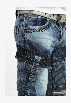 Jeans aus Denim mit einem Farbverlauf in Blau, genagelten Akzenten und einem Riemen mit Schnallen. Strukturierte Oberfläche mit mehreren Taschen und Nähdetails.