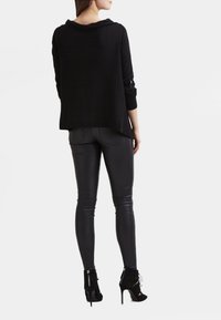 Svart lättviktig tröja med draperad halsringning, kombinerad med svarta figurnära läderbyxor och stövletter med hög klack och textur.