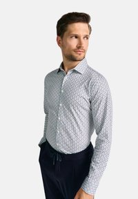 Langärmliges Hemd mit Knopfleiste aus weißem Stoff mit blauem Blumenmuster. Verfügt über einen Kragen und eine schlanke Passform, kombiniert mit marineblauen Hosen.