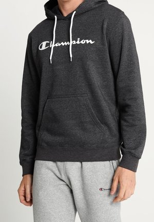 Personne portant un sweat à capuche Champion gris foncé avec des cordons blancs et un pantalon de survêtement Champion gris clair.