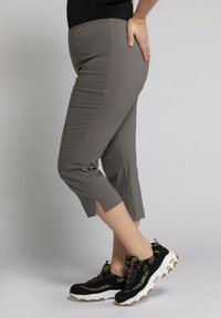 Pantalons gris mi-mollet au design ajusté et fentes latérales, associés à des baskets noires texturées avec des semelles et des lacets blancs.