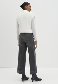 Gilet bianco soffice, jeans grigi a gamba larga, stivaletti neri alla caviglia; i tessuti contrastano con il denim liscio e il morbido tessuto, con risvolti piegati.