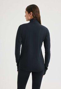 Camiseta deportiva de manga larga en color navy con un cuello alto, costuras planas y un dobladillo trasero ligeramente alargado para mayor cobertura. Tejido suave y elástico.
