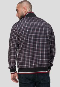 Męska kurtka w kratkę w kolorach czarnym, czerwonym i białym. Posiada gładki czarny rypsowy kołnierz i mankiety z czerwonymi i białymi paskami. Gładka tekstura.