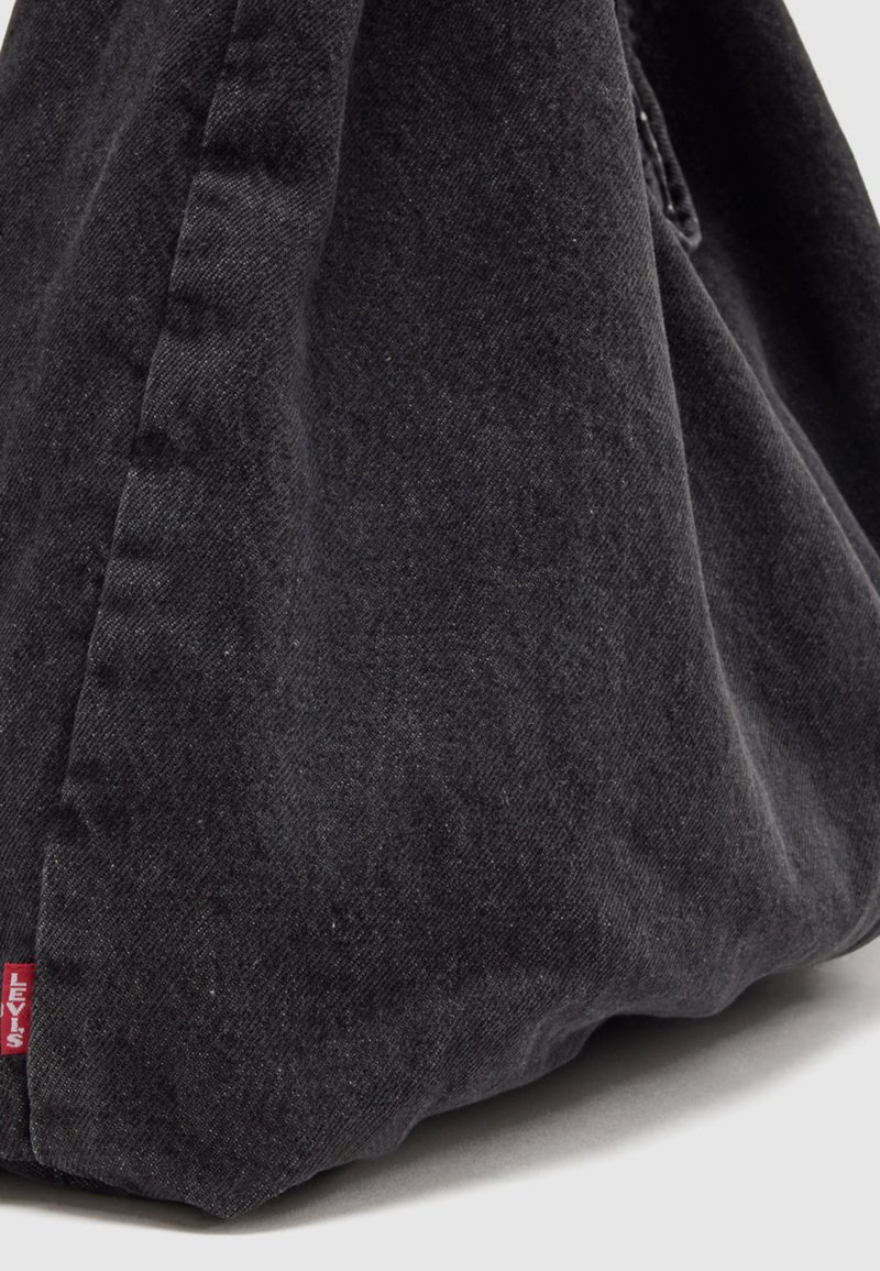 Schwarzer Denim-Stoff mit sichtbaren Nähten und einem kleinen roten Levi's Markenetikett in der unteren linken Ecke.