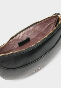 Borsa in pelle nera con superficie testurizzata, chiusura con zip e interno di un rosa chiaro con un'etichetta con logo e un motivo ripetuto sobrio.