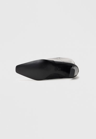 Black leather high-heeled shoe with a pointed toe and a smooth finish. The sole is matte black with a slight ridge for traction.