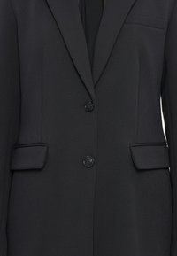 Blazer nero su misura con due bottoni frontali, tasche a pattina e tasca sul petto, mostrato in primo piano frontalmente.