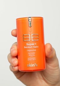 Conteneur orange vif de crème BB avec un couvercle doré brillant, étiqueté "Super+ Beblesh Balm", indiquant des caractéristiques anti-rides et de protection UV.