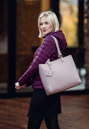 Hellrosa Tragetasche mit glatter Textur, rechteckiger Form und einem markanten Anhänger. Verfügt über verstellbare Schultergurte und metallische Akzente.