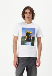 White cotton t-shirt featuring a colorful graphic of a backpack, with yellow accents, set against a blue sky and green landscape.
