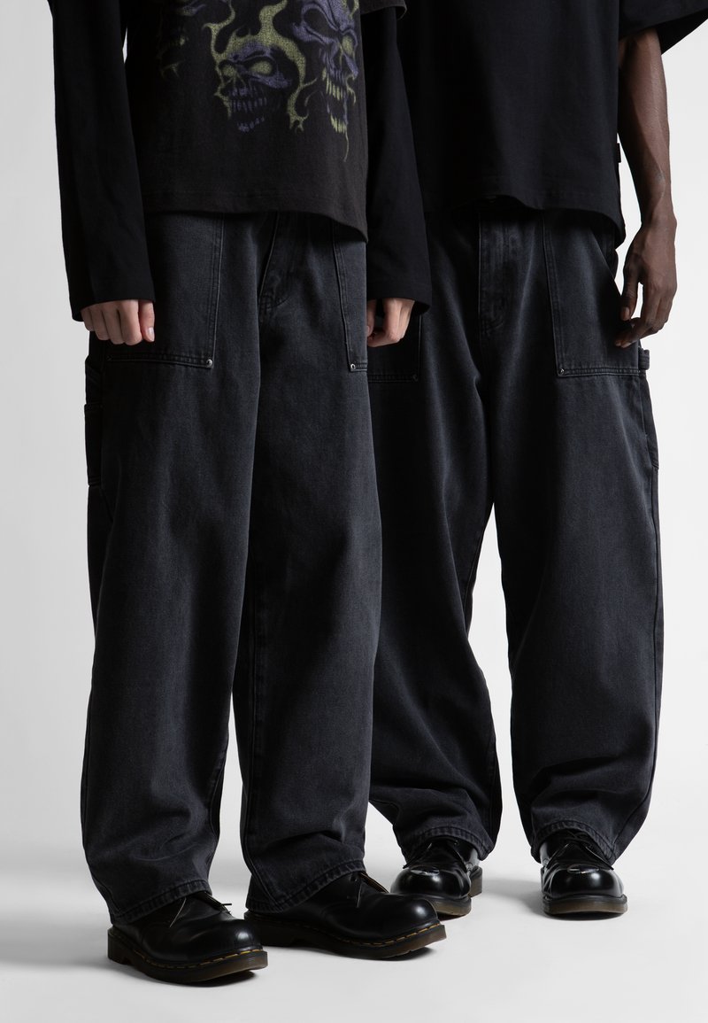 Juodos džinsinės cargo kelnės turi laisvą siluetą, matomas kišenes ir siuvinėjimą. Renkamos su juodais batais, papildytos grafika puoštomis juodomis marškinėliais.