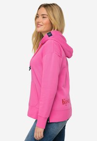 Felpa rosa con tasca a marsupio, cappuccio con cordino e dettagli ricamati. Presenta un accento blu navy sulla spalla e polsini a coste.