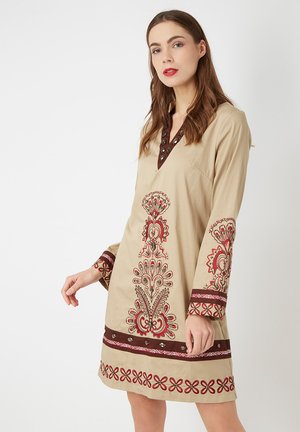 Vestido túnica beige con bordados rojos y acentos marrones. Presenta un escote en forma de V con botones decorativos y mangas largas con puños estampados.