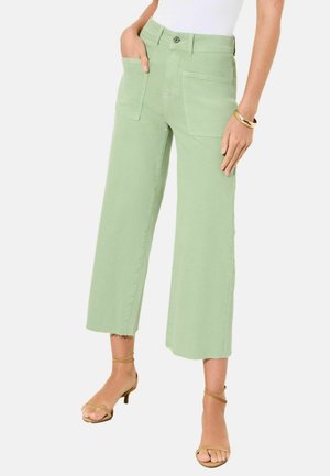 Frau trägt hellgrüne, weit geschnittene, gekürzte Hosen mit aufgesetzten Taschen vorne und sandfarbene, verzierte Sandaletten mit Absatz.