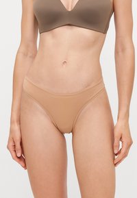 Beige naadloze ondergoed in een lage taille, thongstijl met een gladde textuur en een minimalistisch ontwerp, gekenmerkt door een dunne tailleband.